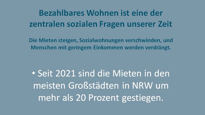 Das Foto zeigt ein Plakat mit dem Titel "Bezahlbares Wohnen ist eine der zentralen sozialen Fragen unserer Zeit". Es werden drei Hauptaussagen in Form von Bullet Points präsentiert: Seit 2021 sind die Mieten in den meisten Großstädten in Nordrhein-Westfalen (NRW) um mehr als 20 Prozent gestiegen. Der Bestand an Sozialwohnungen in NRW ist von 1,3 Millionen (1990) auf aktuell 422.000 gesunken. 2024 wurden in NRW 122.170 wohnungslose Menschen offiziell erfasst. Unterhalb des Textes befindet sich das Logo der Organisation "Wir wollen wohnen" und die zugehörige Webseite "www.wir-wollen-wohnen-nrw.de".