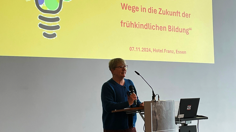 Auf dem Foto ist Britta Altenkamp zu sehen, die an einem Rednerpult steht und in ein Mikrofon spricht. Hinter ihr ist eine Leinwand mit einer Präsentation projiziert, auf der der Titel „Vision Kita: Wege in die Zukunft der frühkindlichen Bildung“ und das Datum „07.11.2024, Hotel Franz, Essen“ zu lesen sind.